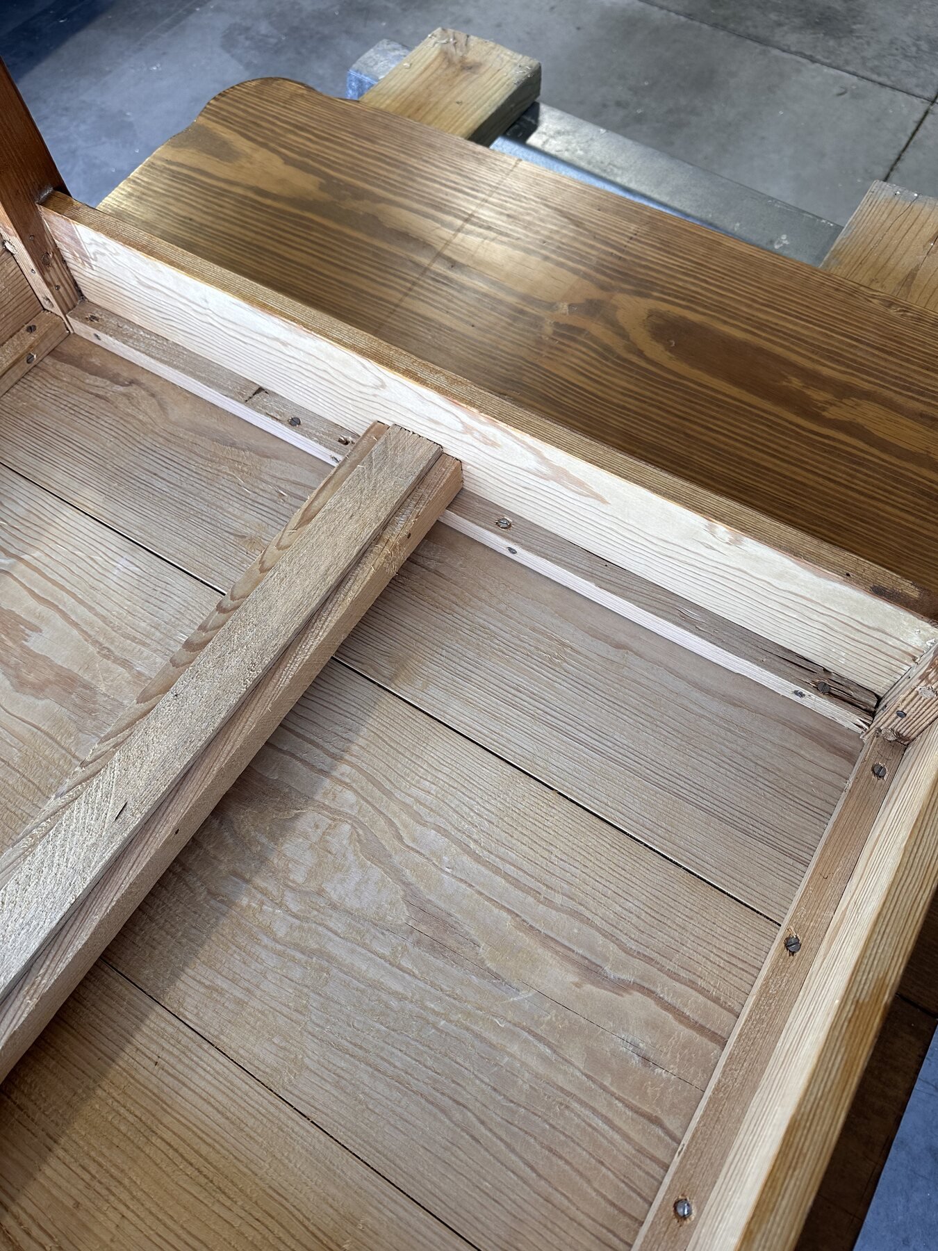 Underside corner showing base rails, perimeter screws, and a wooden leaf-support brace