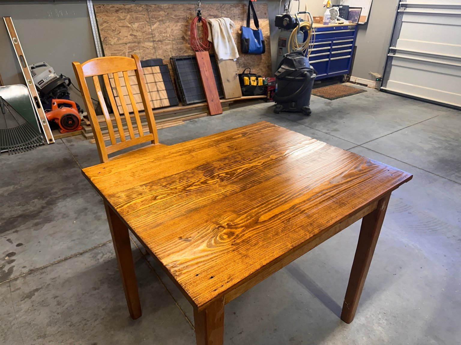 Whole table in the garage after its first polyurethane coat, with a bright reflection across the stained top