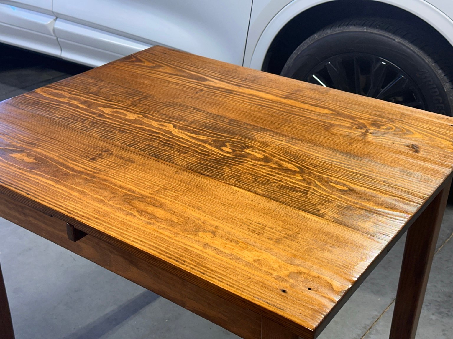 Opposite view of the glossy stained tabletop beside the parked white vehicle