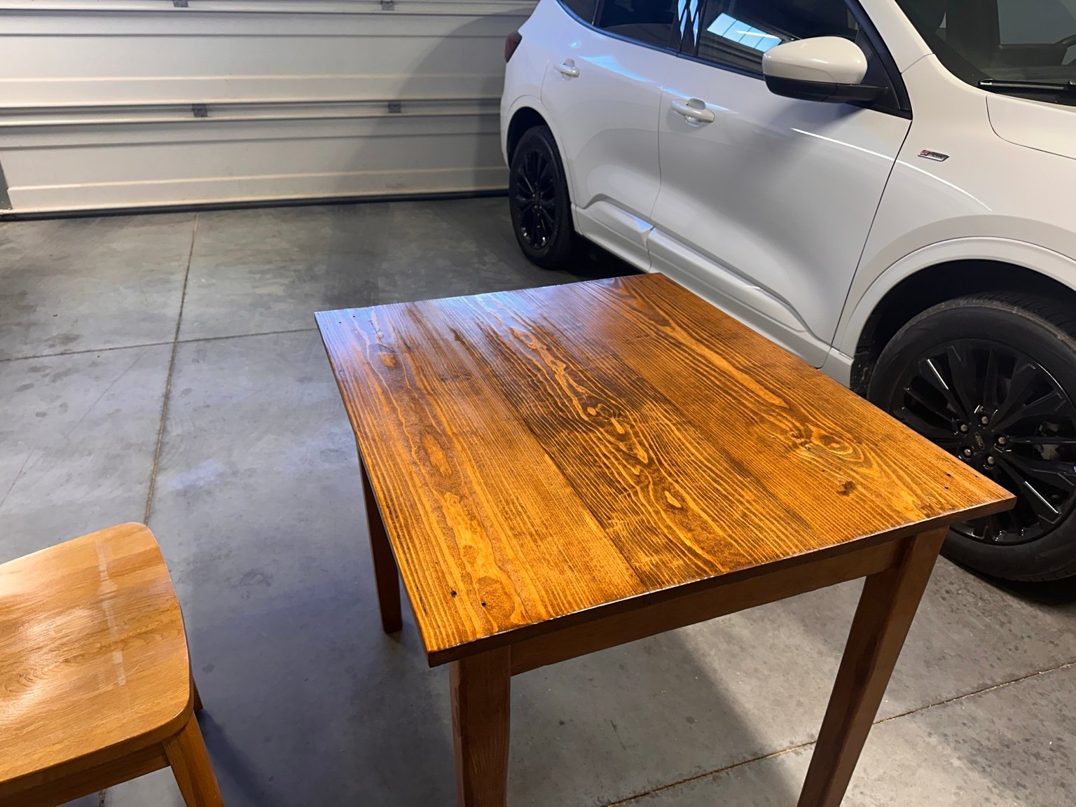 Table with its first clear coat standing beside a white vehicle and the garage door