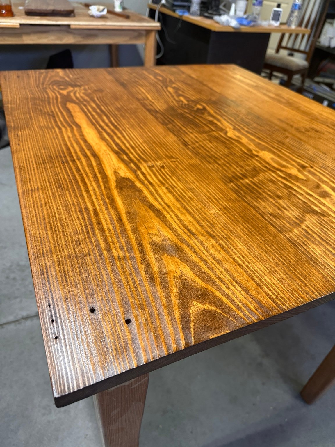 Angled view along the tabletop edge showing sheen, grain, and several small old holes