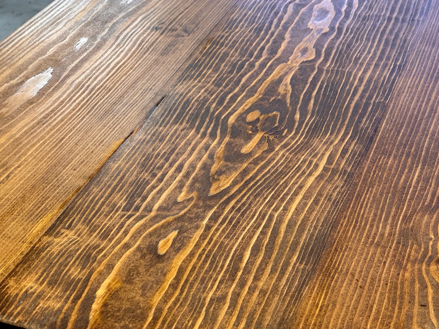 Close-up of a dark knot and surrounding amber grain beneath the third polyurethane coat