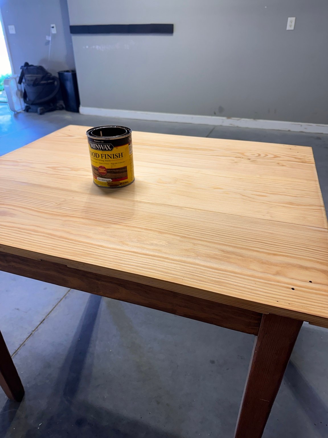 Pale sanded tabletop above the darker apron and legs, with a stain can on top