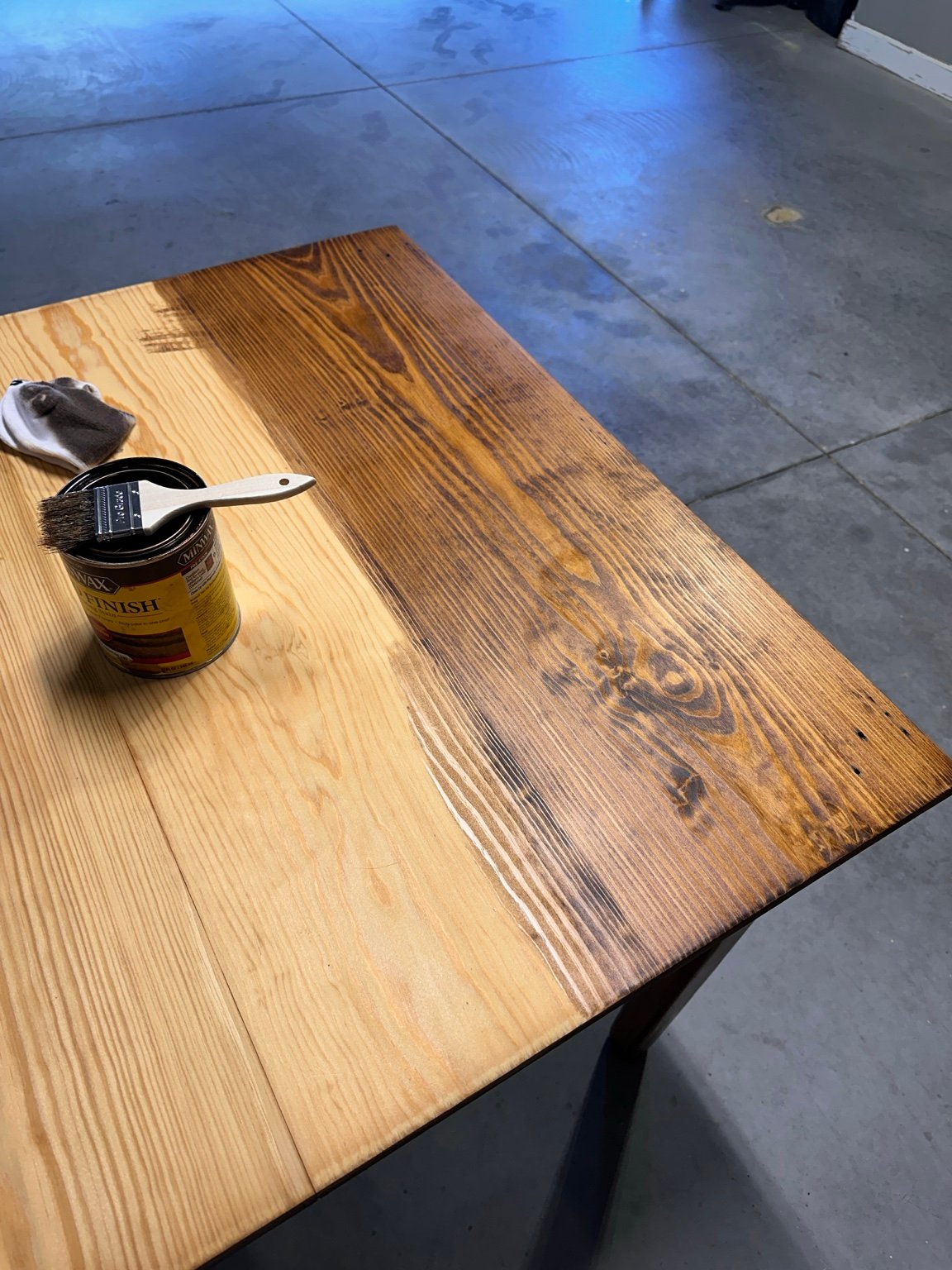 Tabletop partly stained dark brown beside bare wood, with brush and stain can nearby
