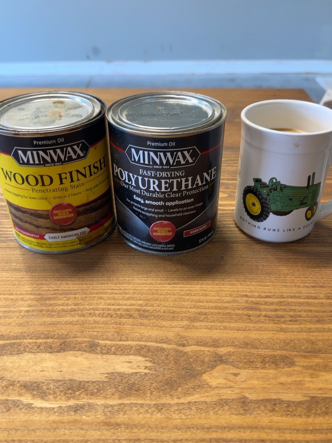 Early American 230 stain and Warm Gloss polyurethane cans beside a John Deere tractor mug