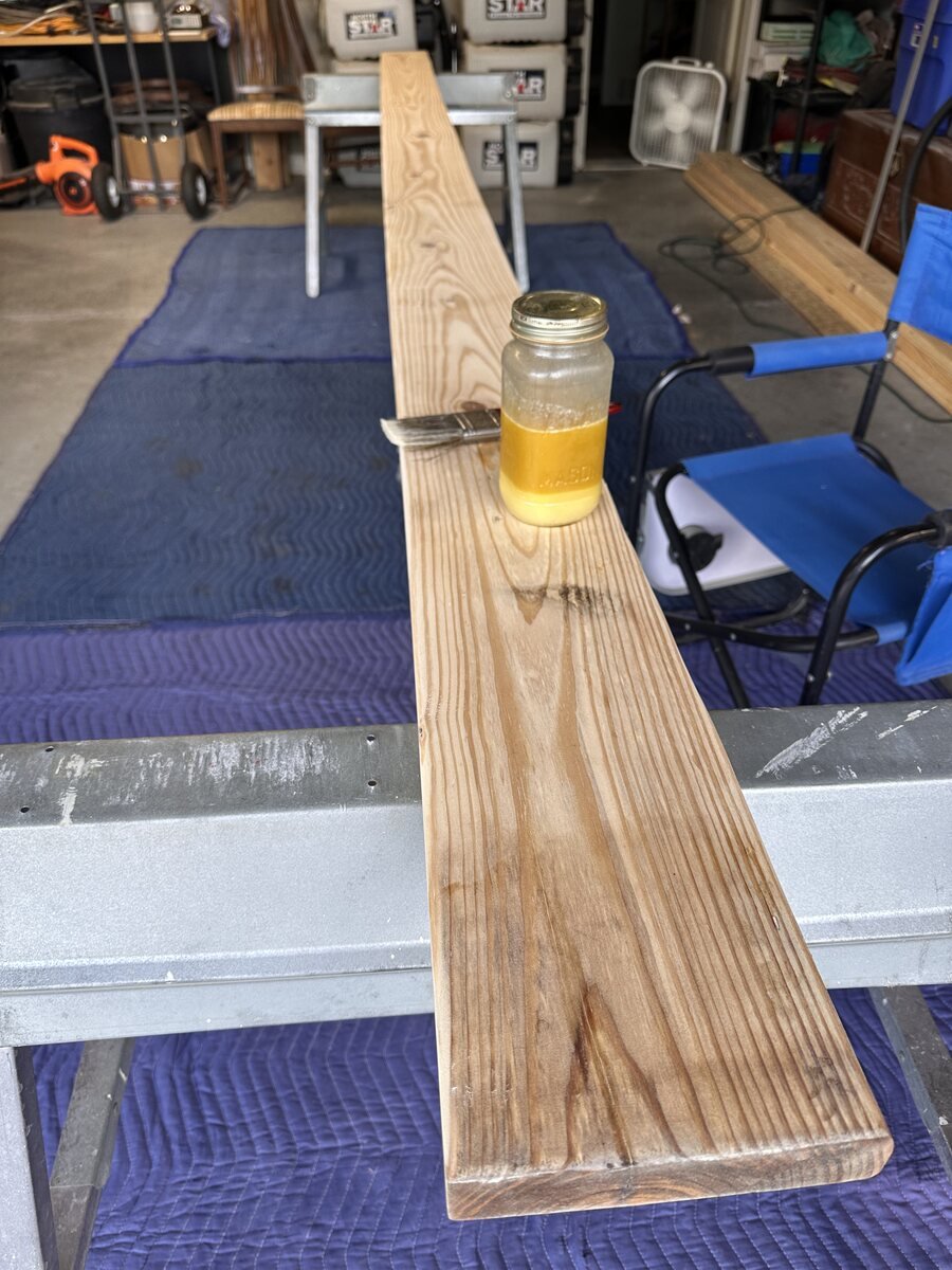 Jar of wood finish and brush resting on the long pine board