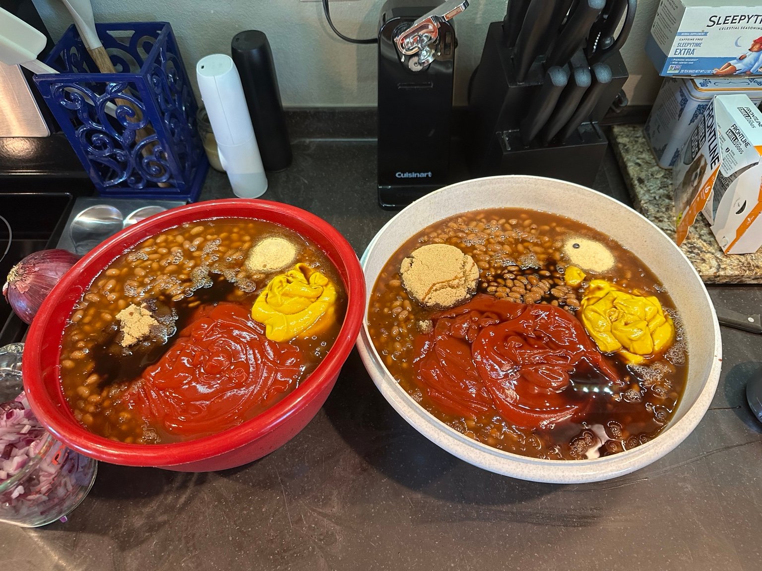 Two bowls of beans topped with brown sugar, ketchup, mustard, and seasonings before mixing