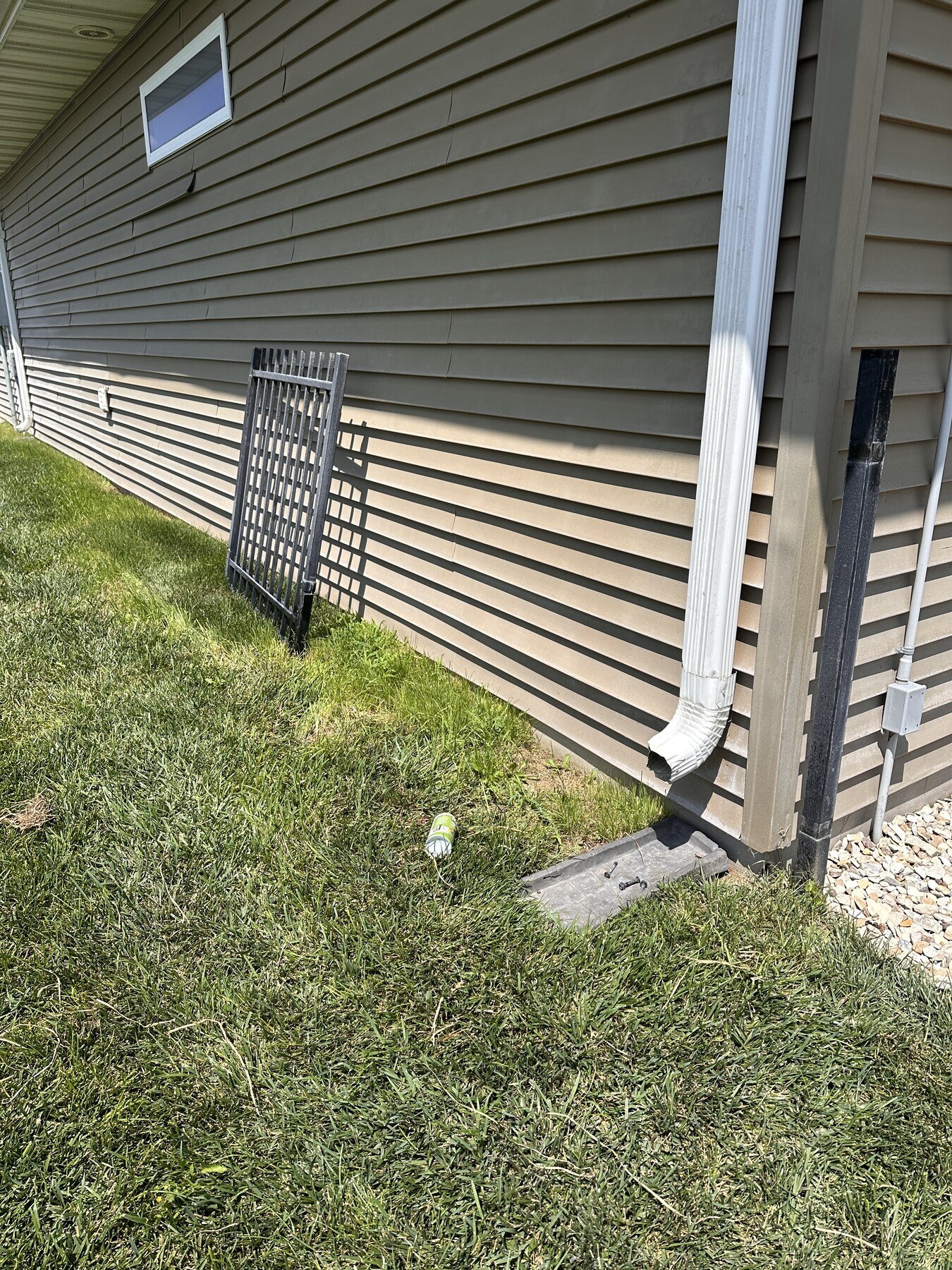 Black metal gate removed from the opening and leaning against the side of the house